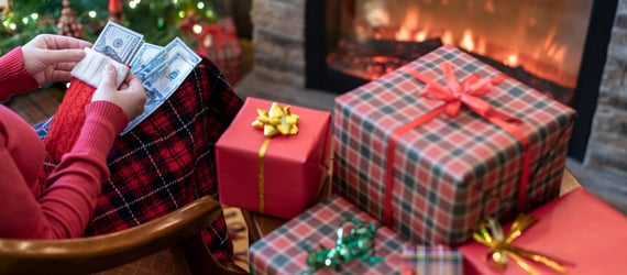 Photo of a woman holding money near a pile of Christmas gifts.