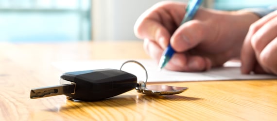 Photo of someone signing auto loan paperwork next to a set of keys. Photo of someone signing auto loan paperwork next to a set of keys.