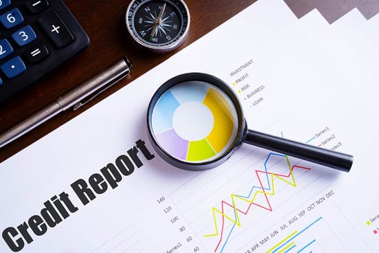 Magnifying glass on colorful pie chart with Credit report text on paper, dice, spectacles, pen, laptop calculator on wooden table - business, banking, finance and investment concept