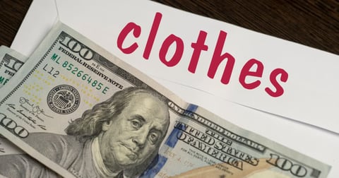 White envelope with the inscription clothes and dollar bills lie on a wooden table. Manage your finances and save money concept. White envelope with the inscription clothes and dollar bills lie on a wooden table. Manage your finances and save money concept.