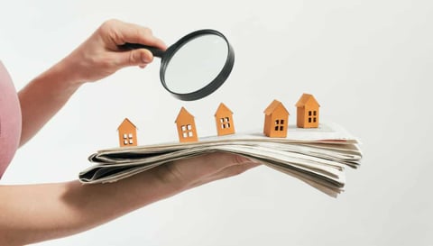 Woman holding a newspaper and magnifying glass, searching for housing concept.
