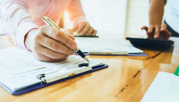 Person holding a pen signing a document on a wooden table.