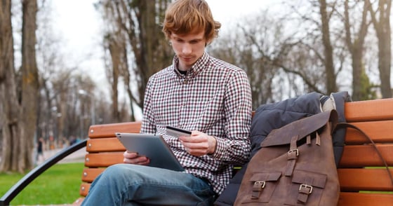 Student sitting on a park bench looking at a credit card Student sitting on a park bench looking at a credit card
