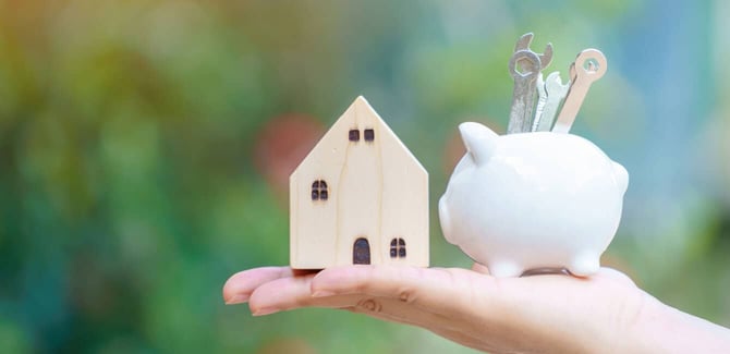 A hand holding a small wooden home and a piggy bank with tools, home renovation loan concept A hand holding a small wooden home and a piggy bank with tools, home renovation loan concept